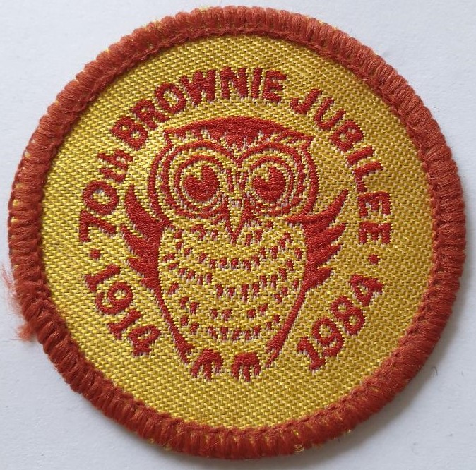 Round woven badge in gold with brown edging. Centre features owl in brown stitching, surrounded by text: 70th Brownie Jubilee 1914 1984