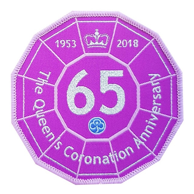 Purple 12-sided badge with lilac edging and silver lettering. Central logo '65' and Girlguiding badge. Outer divided into compartments in lilac thread. Text: The Queen's Coronation Anniversary 1953 2018