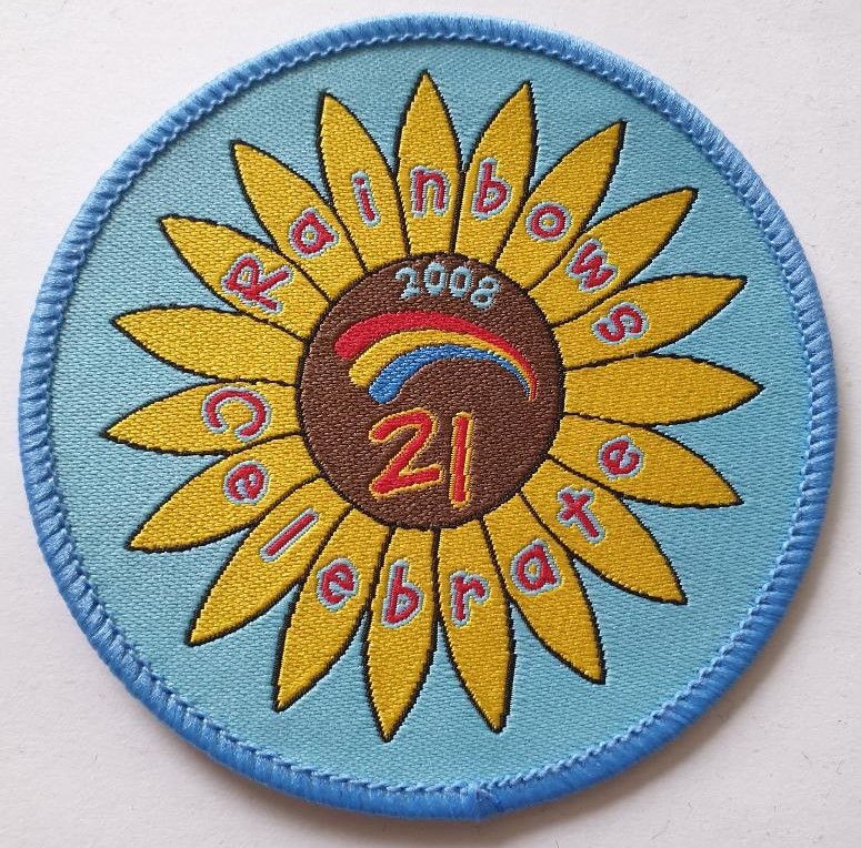 Rainbow 21st Anniversary badge with a sunflower design on a light blue ground
