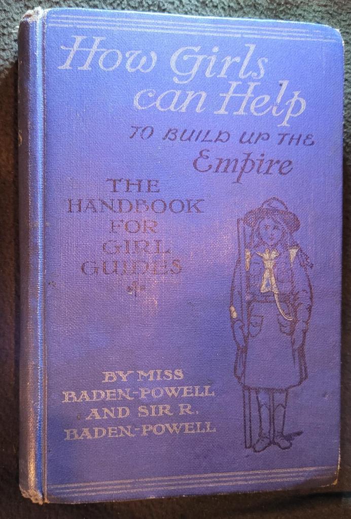 Image of hardback handbook titled "How Girls Can Help to Build Up the Empire" by Agnes Baden-Powell, with drawing of Girl Guide on cover