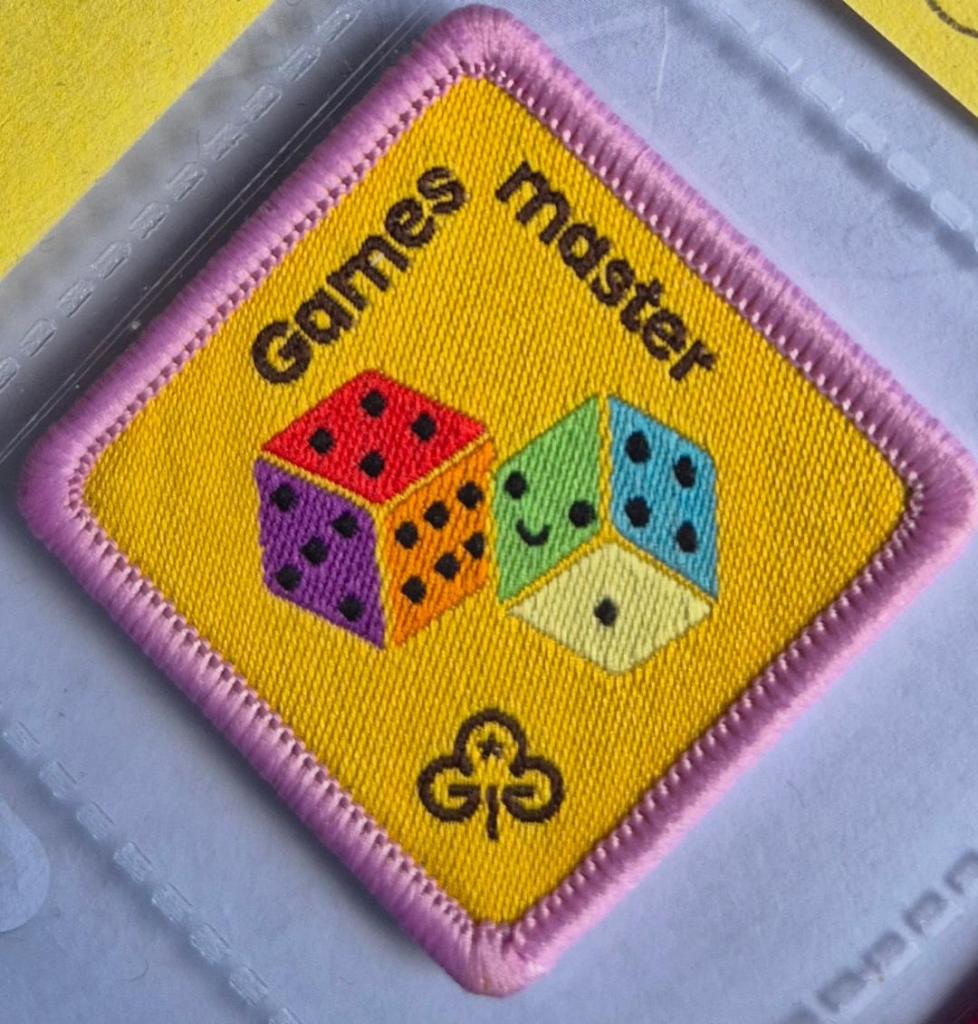 Brownie Games Master badge, light pink binding, logo is two dice