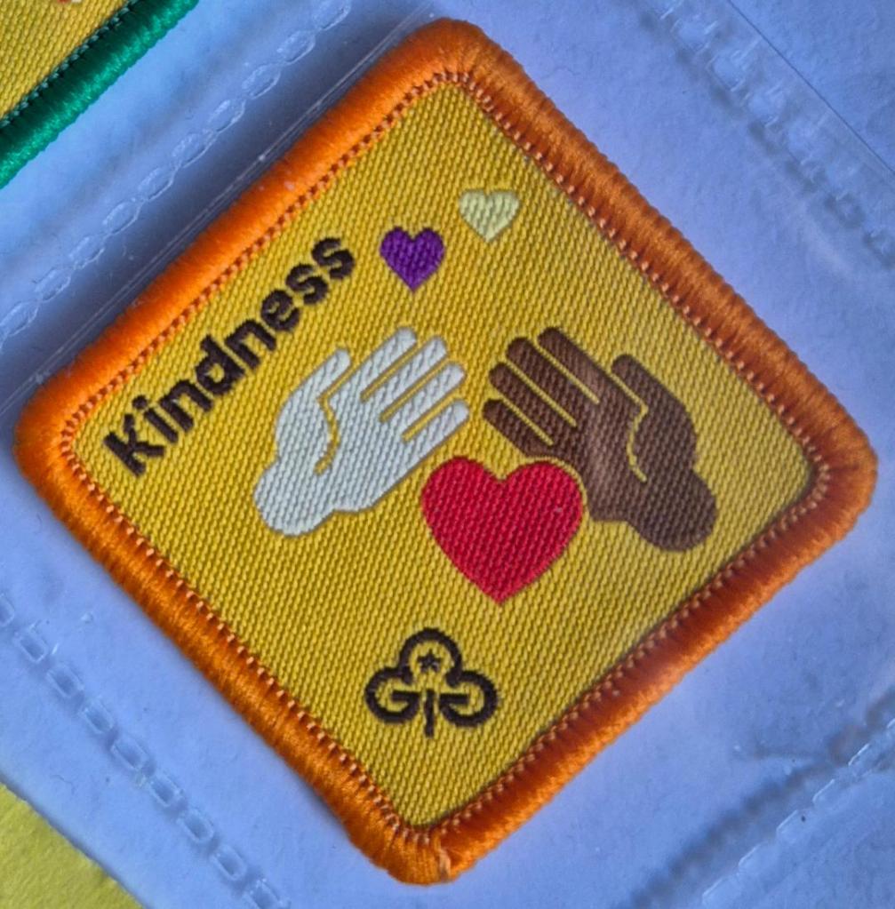 Brownie Kindness badge, orange binding, two hands and heart logo.