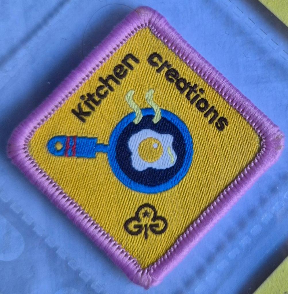 Brownie Kitchen Creations badge, light pink binding. Egg in frying pan logo