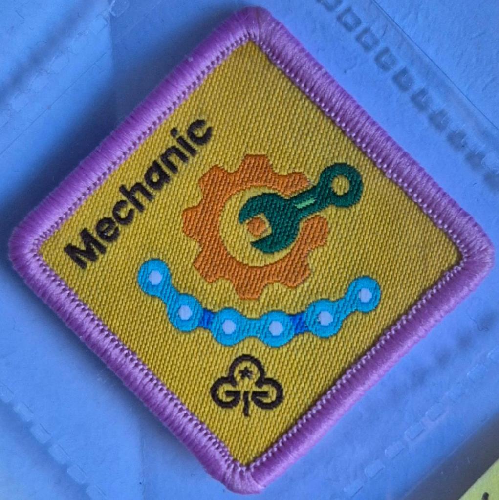 Brownie Mechanic badge, light pink binding. Spanner and bicycle chain logo.