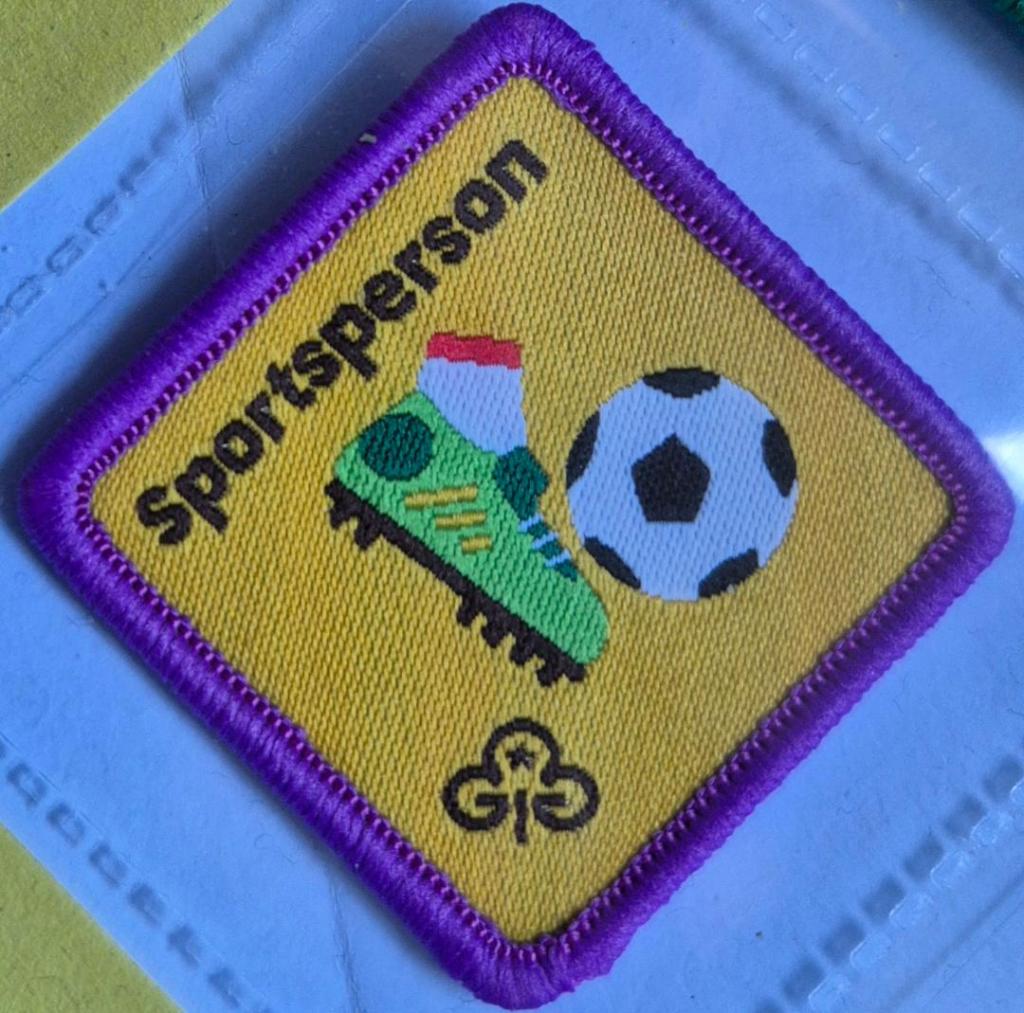 Brownie Sportsperson badge, purple binding. Booted foot kicking football logo.