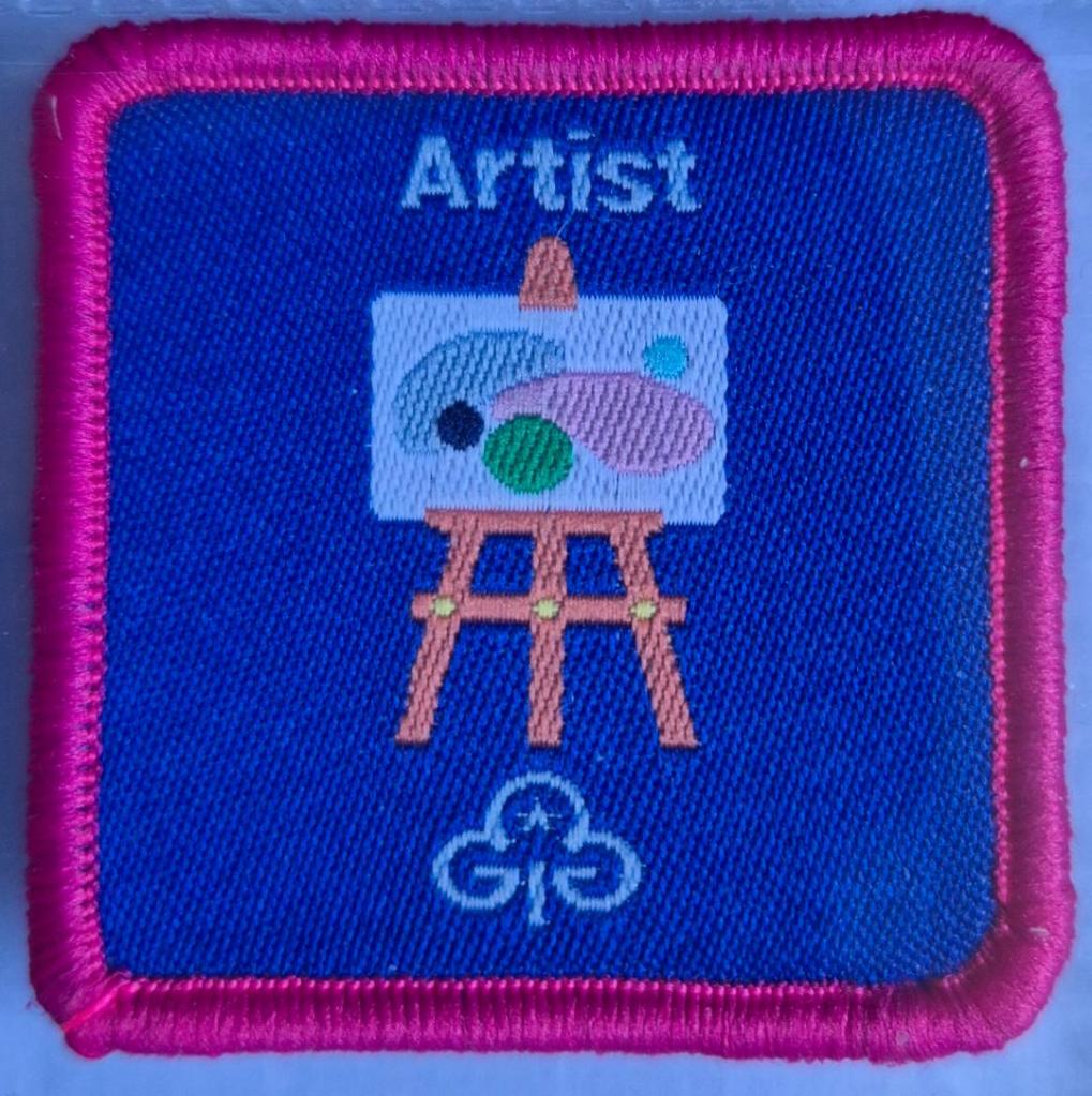 Guide Artist badge with dark pink binding.  Picture on easel logo.
