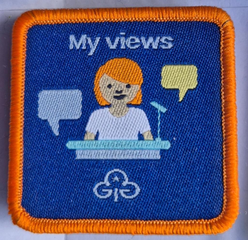 Guide My Views badge, orange binding.  Girl at platform with speech bubbles logo.