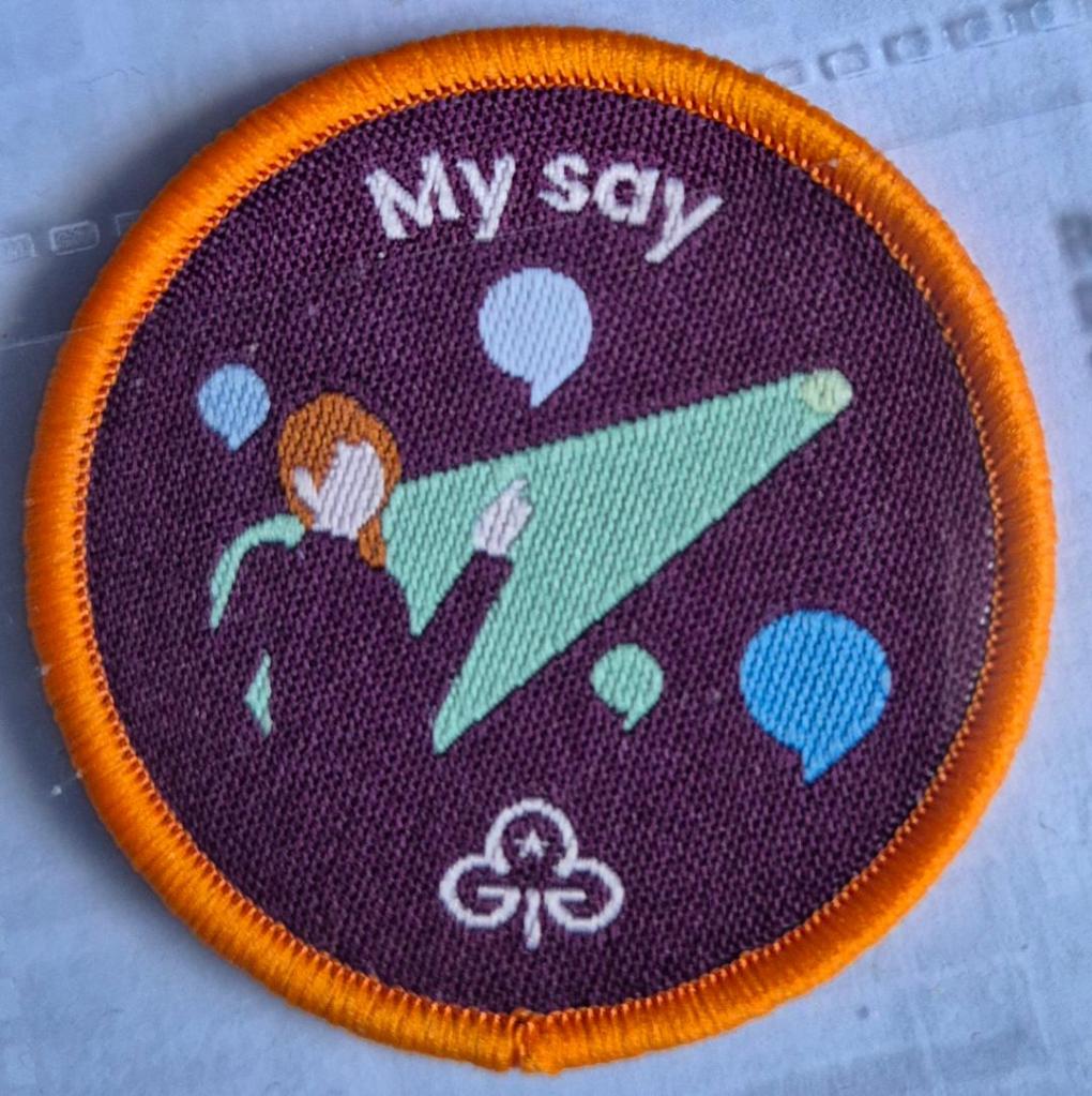 Ranger My Say badge, orange binding.  Figure in spotlight surrounded by speech bubbles logo.